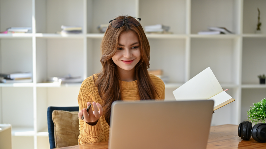 Freelance professional engaging in a virtual meeting, holding a notebook and smiling while working remotely from a cozy home office.